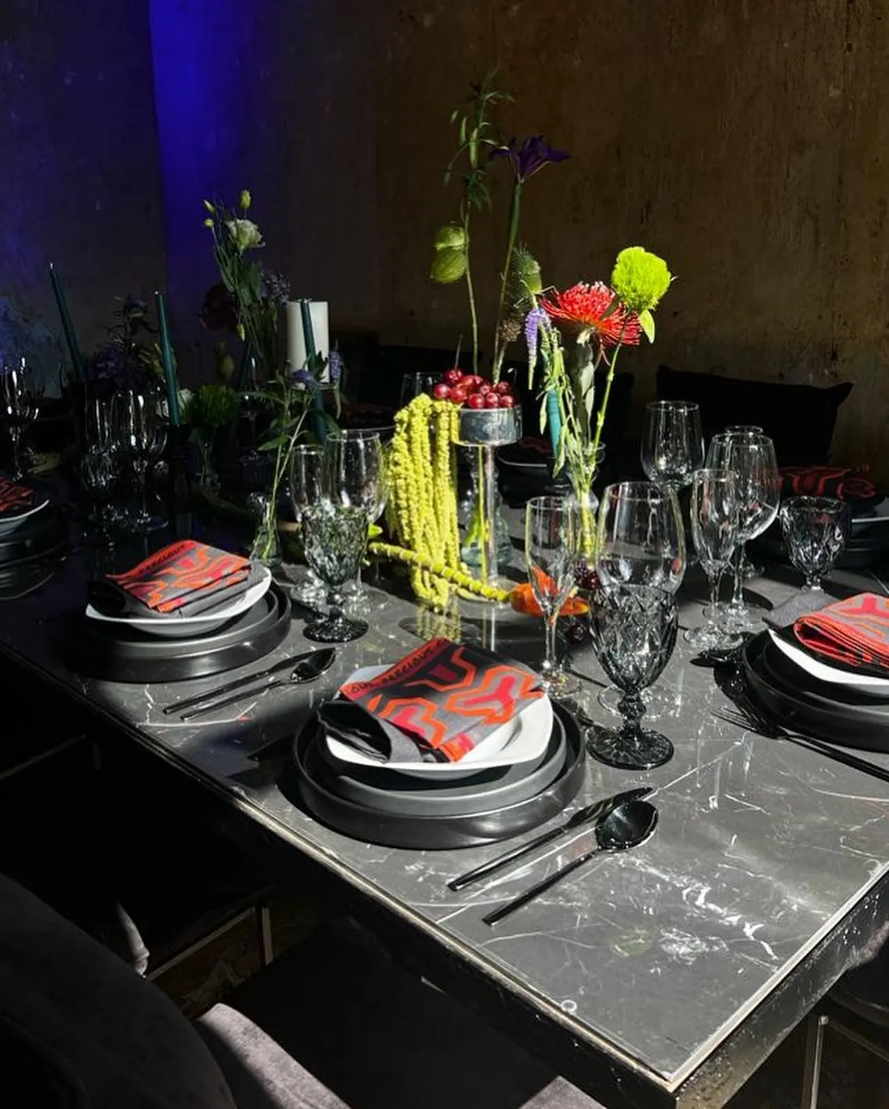 A dark stone table set with red napkins, glassware and sculptural yellow and pink flowers