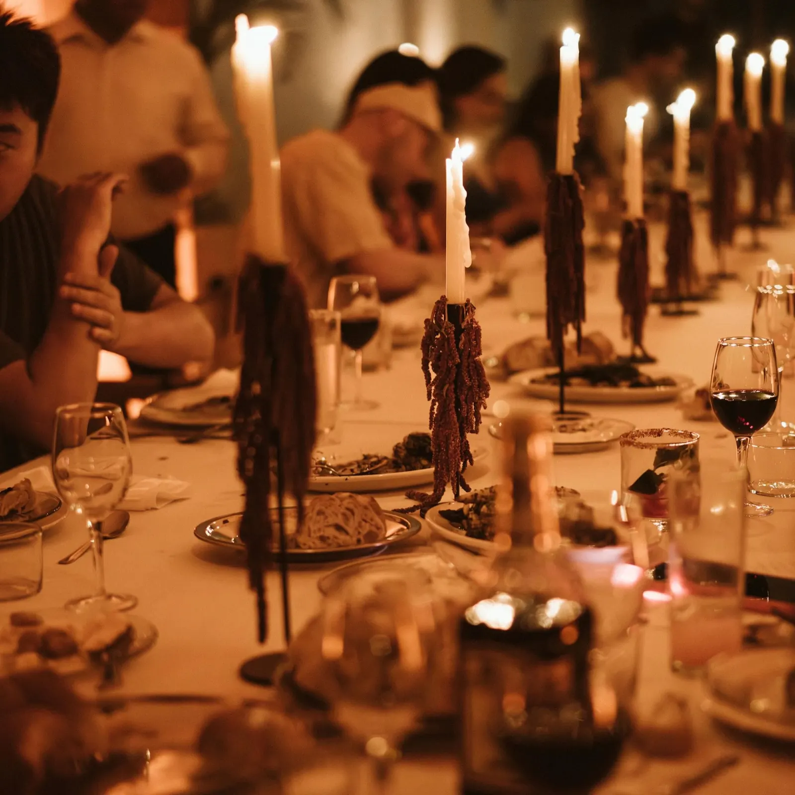 Candlelit dinner table with tall tapers, wine glasses and flowers in warm light