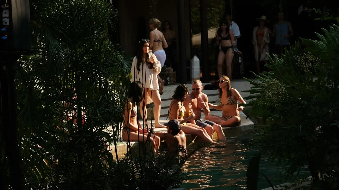 Guests sitting and talking by a pool surrounded by tropical plants